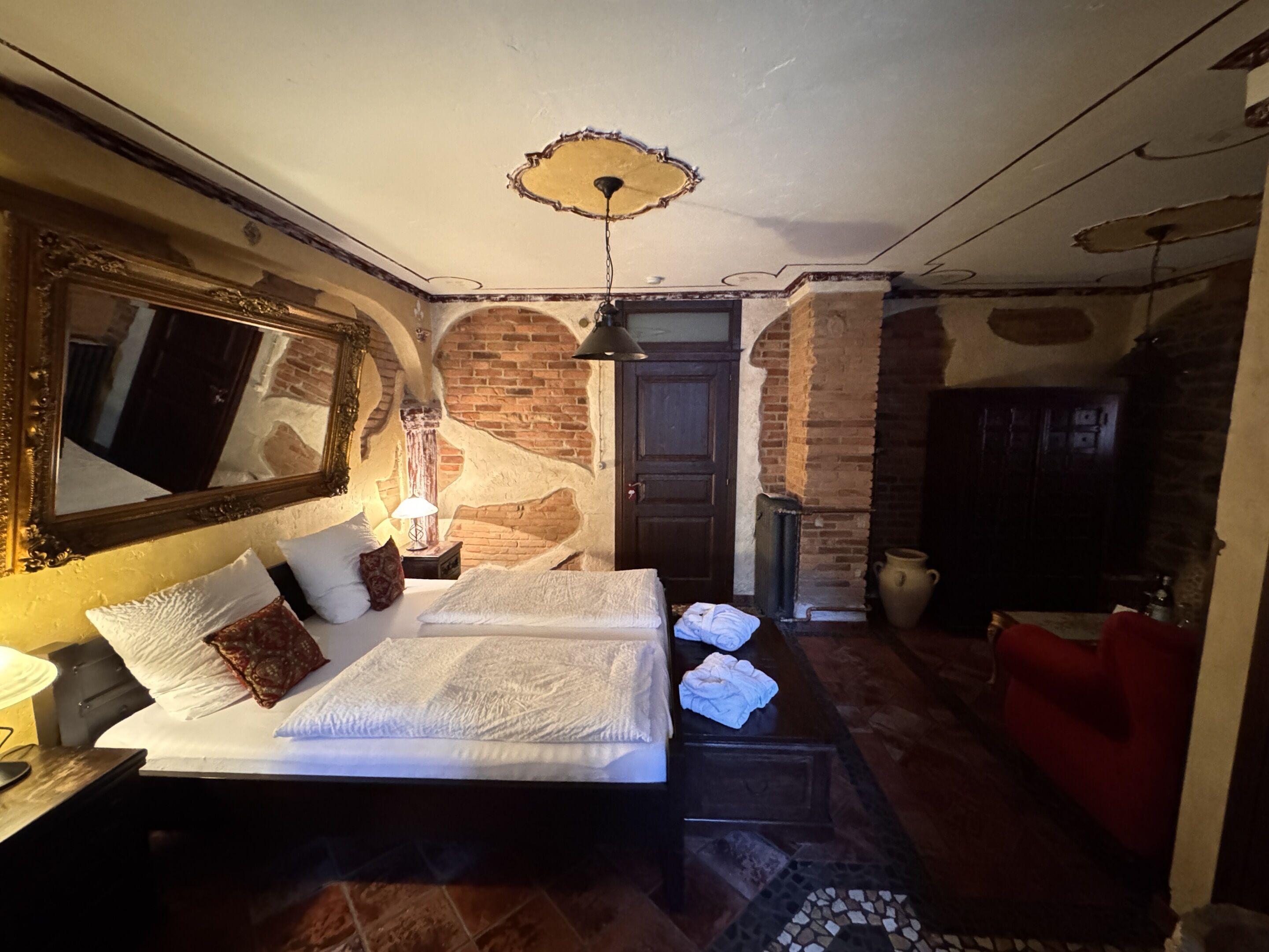 A bedroom with a large bed, a mirror, a lamp, and a fireplace.