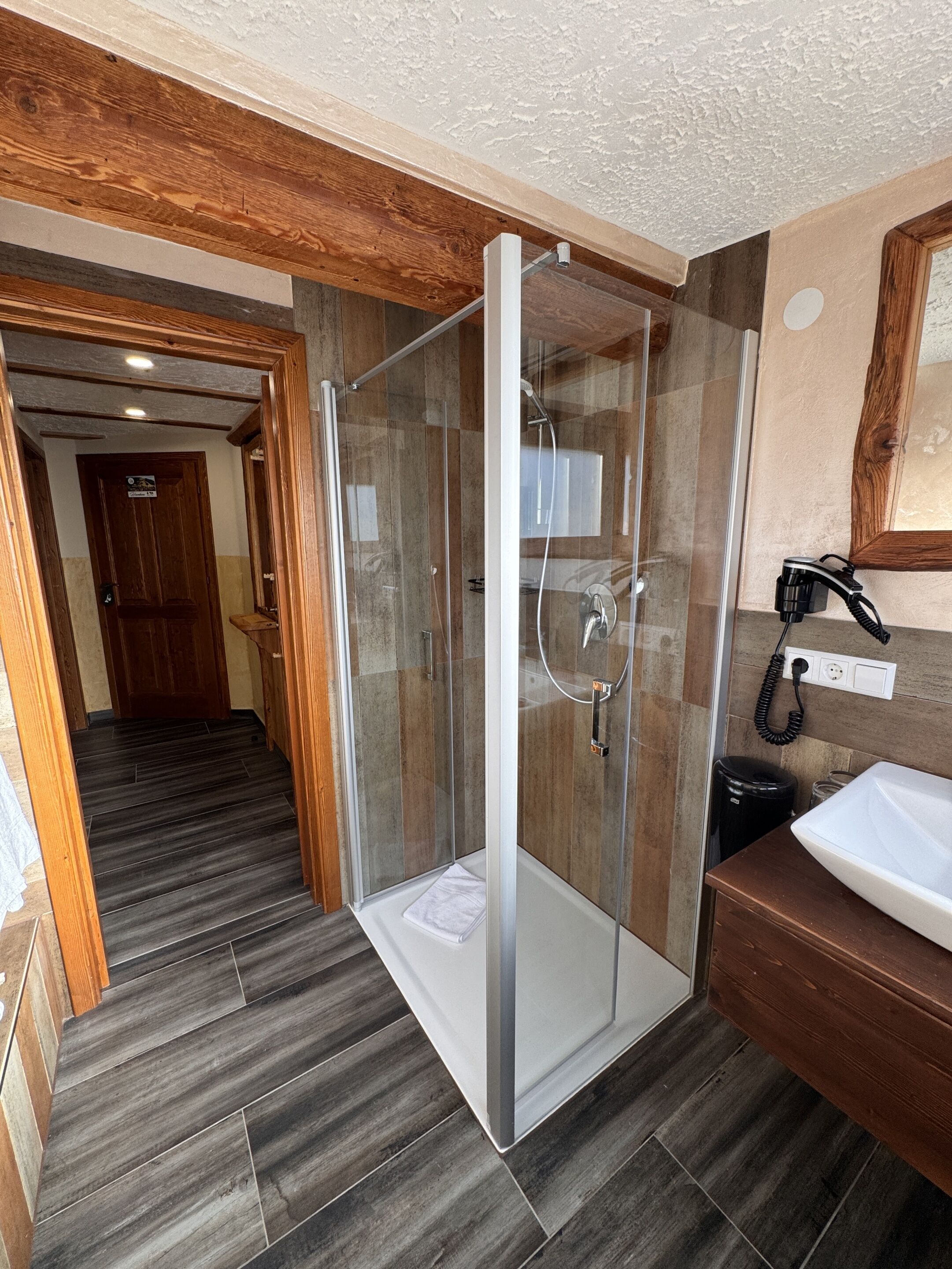 A modern bathroom with a glass-enclosed shower, a wooden vanity, and a tiled floor.