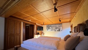 Een slaapkamer met houten vloer, een bed, kussens, een bureau en een televisie.