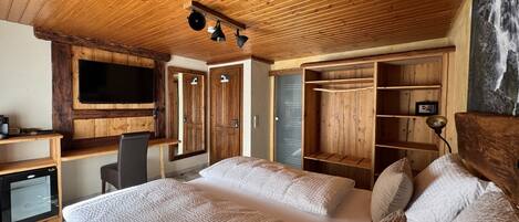A wooden-themed bedroom with a bed, a desk, a chair, a television, and a wardrobe.