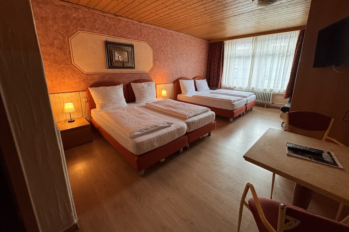 Una habitación de hotel con dos camas, techo de madera, una mesita y una silla.