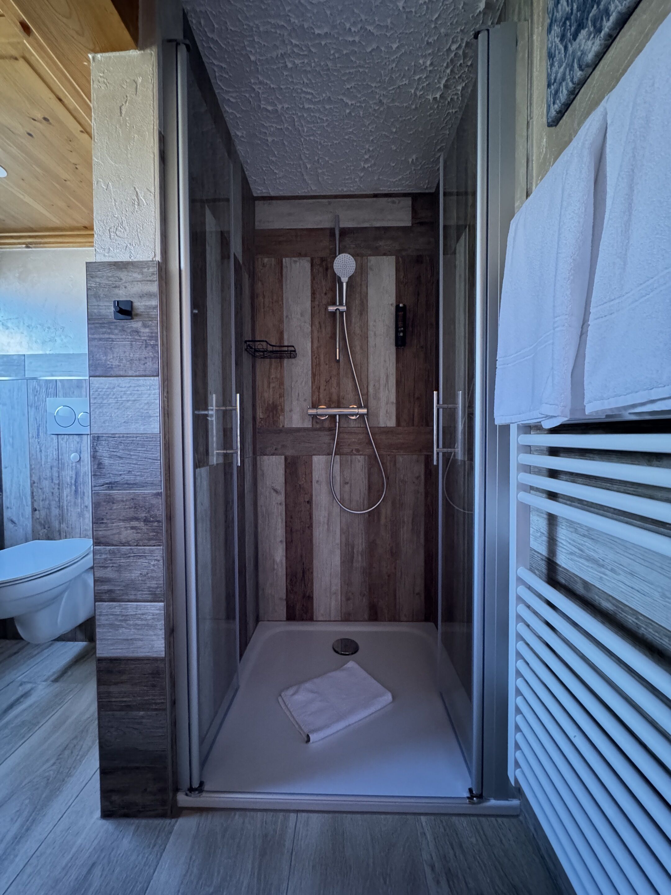 Ein modernes Duschbad mit Glasabtrennung, Holzvertäfelung und einem weißen Handtuch auf der rechten Seite.