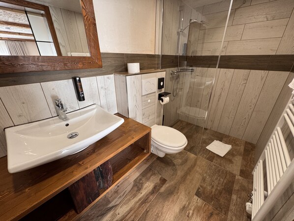 A modern bathroom with a wooden vanity, a white sink, a toilet, and a glass shower enclosure.