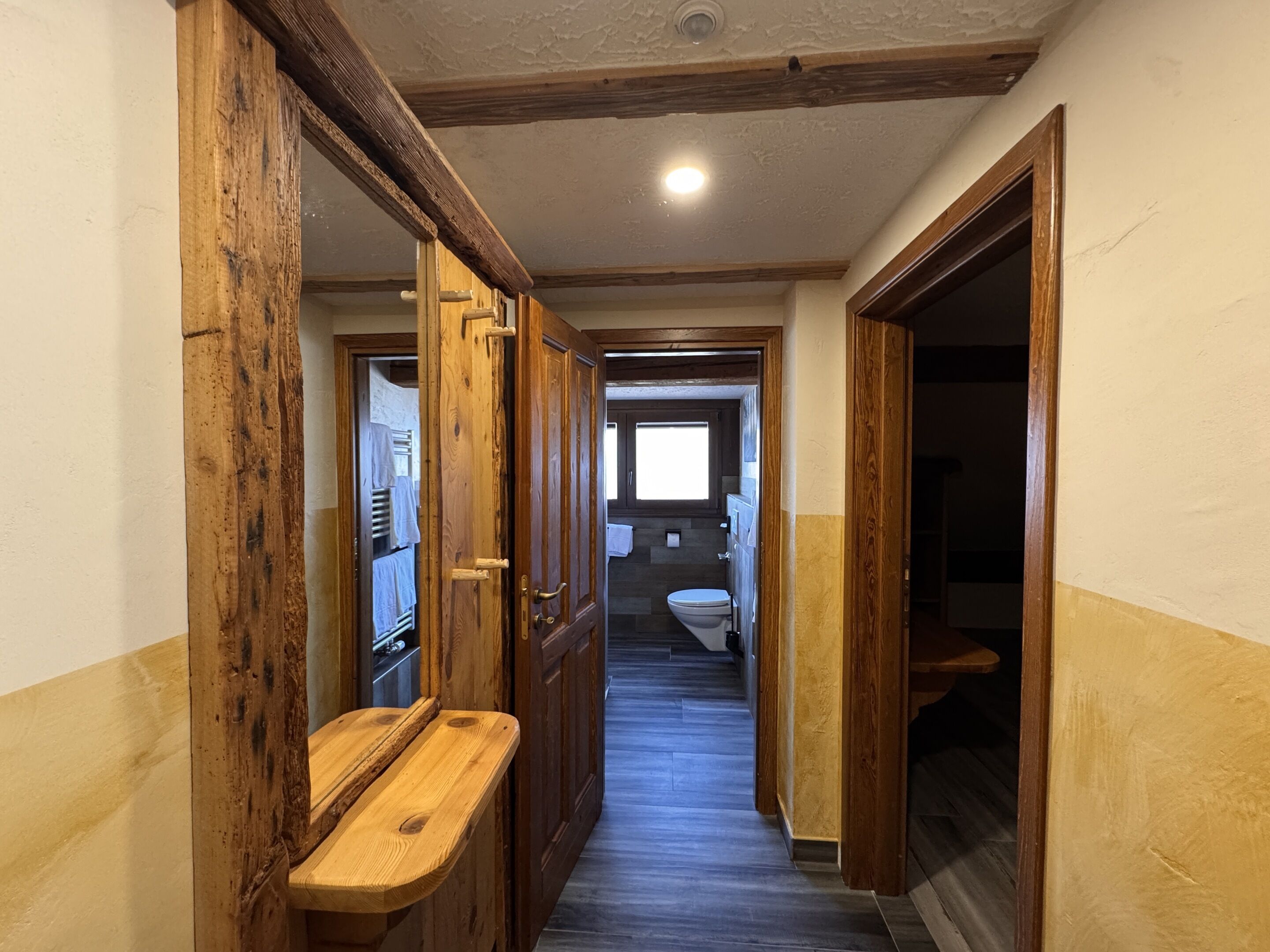 Ein Flur mit Holztüren und einer Bank, der zu einem Badezimmer mit Toilette und Fenster führt.