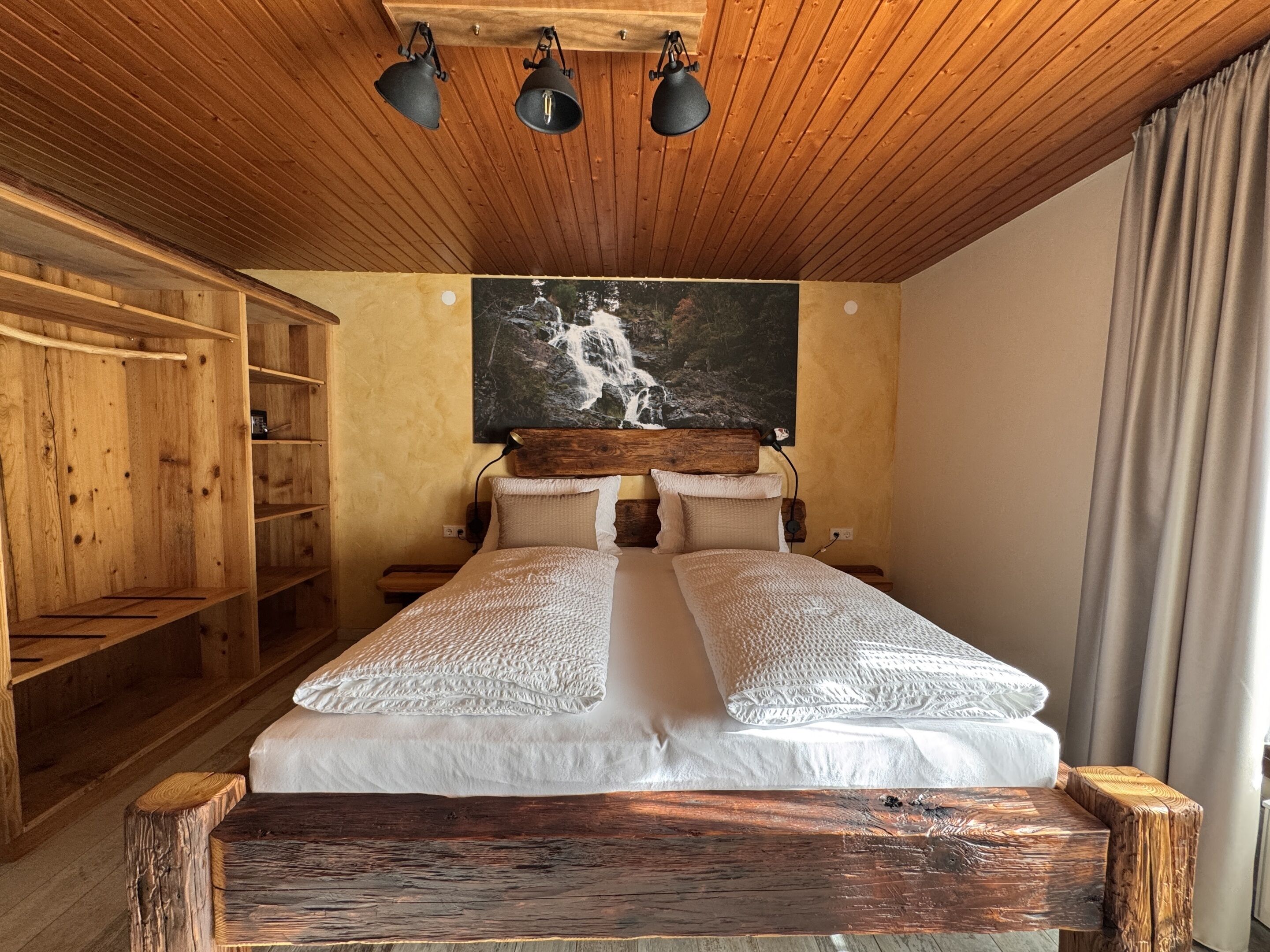 Un dormitorio de madera con una cama, dos almohadas, un cabecero y un cuadro de una cascada.