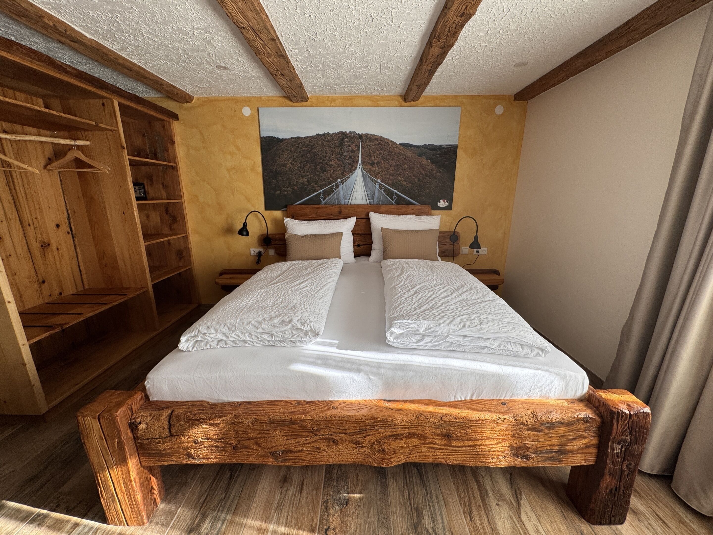 A wooden bed with a headboard, two bedside tables, a wooden wardrobe, and a painting of a landscape on the wall.