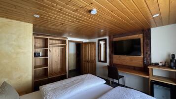 Un dormitorio con techo de madera, una cama con ropa blanca, un televisor montado en la pared y un escritorio de madera con una silla.