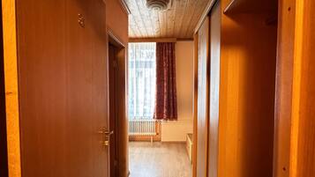 Een houten gang met een radiator, een raam met gordijnen en een deur aan de linkerkant.