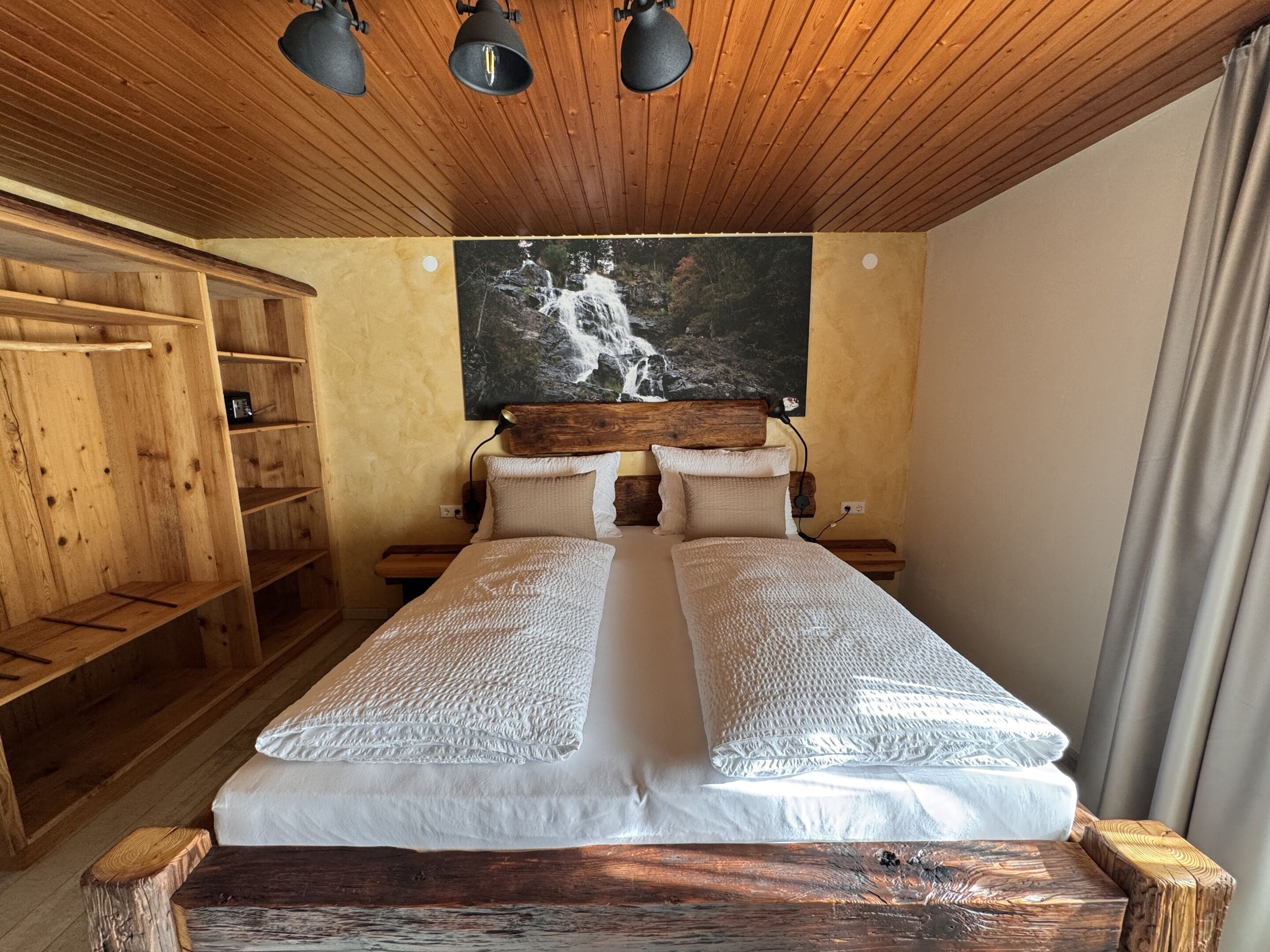 A wooden room with a bed, wooden shelves, and a painting of a waterfall.