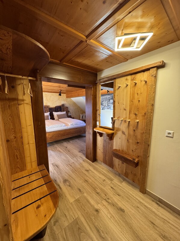 Un interior de madera con una cama, un banco y una puerta con ganchos.