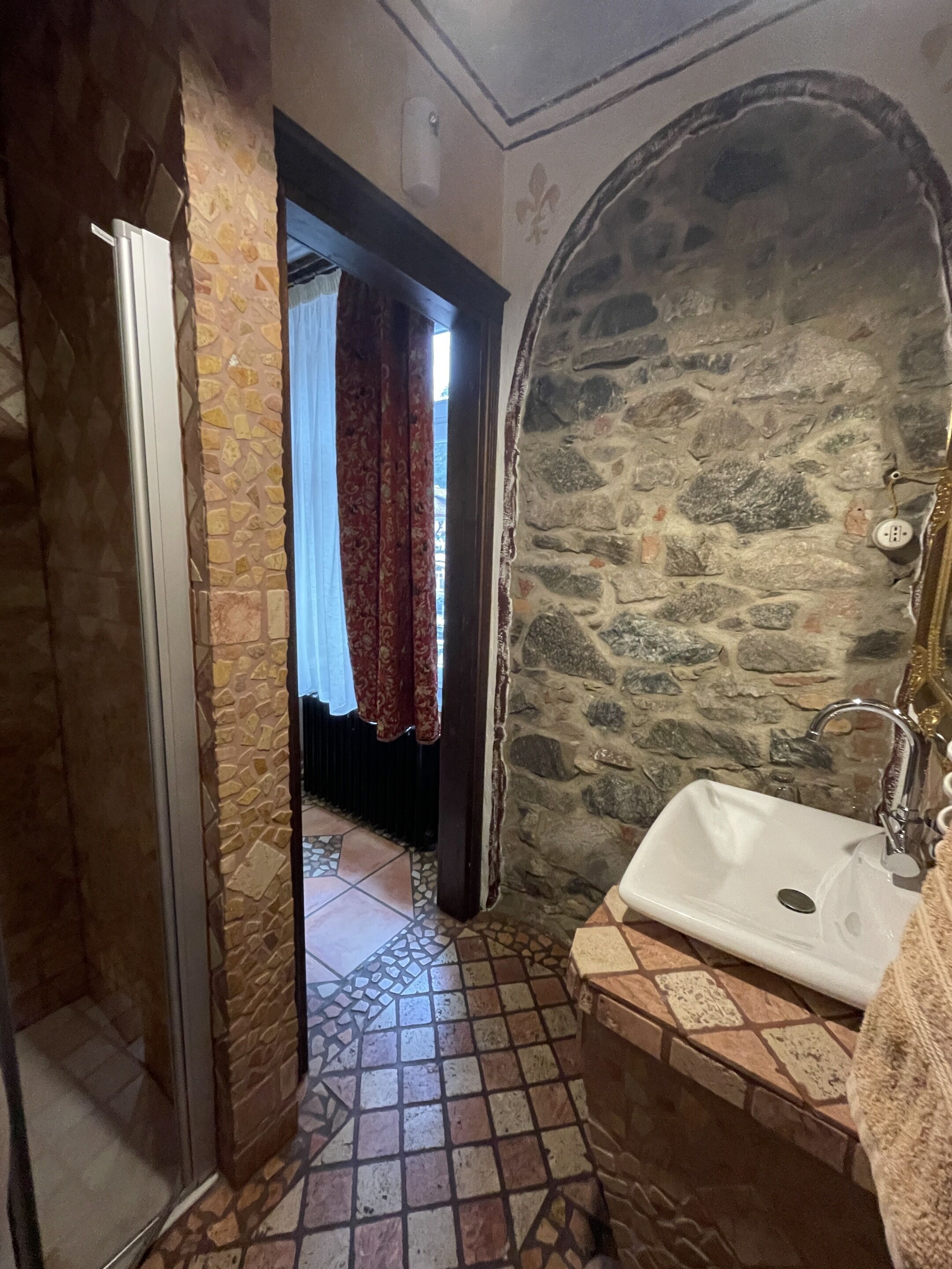 Un baño con pared de piedra, piso de baldosas, lavabo blanco y zona de ducha.