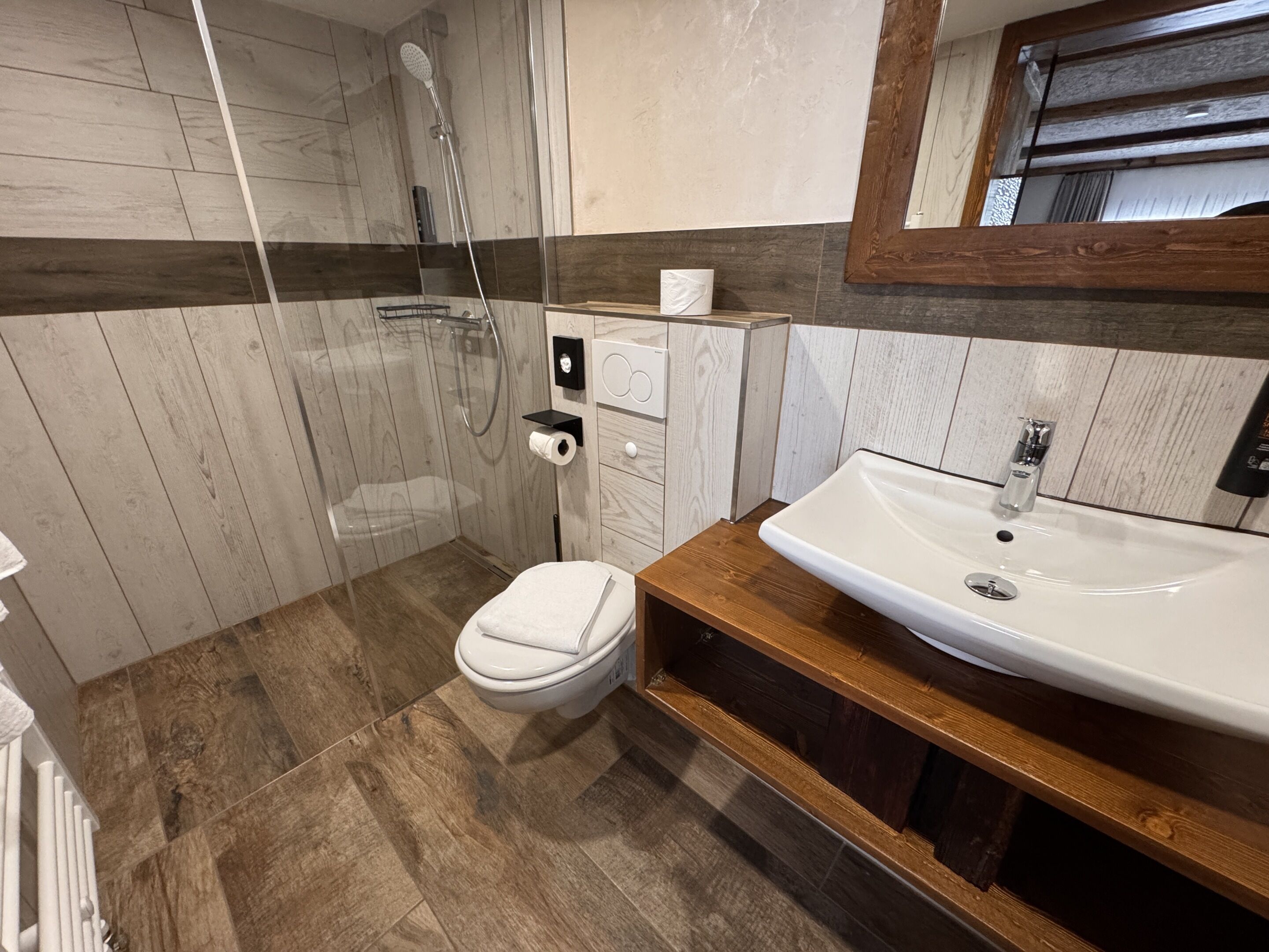 A modern bathroom with a wooden vanity, a white sink, and a shower area.