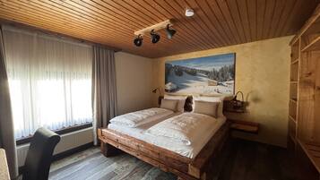 Techo de madera, una cama con sábanas blancas, un cuadro de un paisaje nevado y una silla.