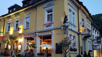 Un edificio amarillo con un letrero que dice 'Pizzeria', mesas al aire libre y una bandera.