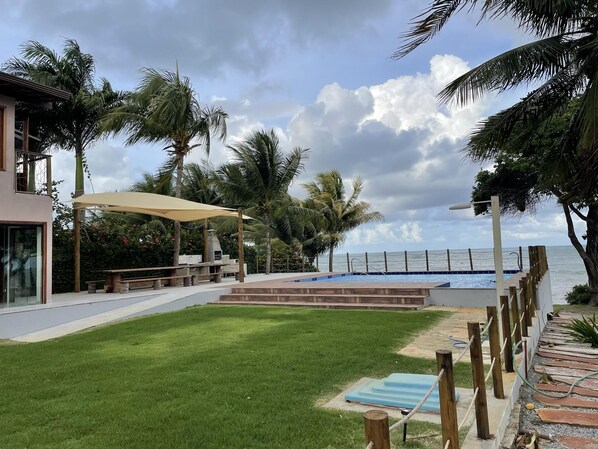 A pool area with a view of the ocean, surrounded by palm trees and a modern building.