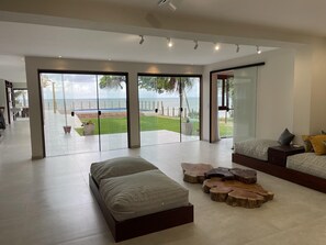 A spacious living area with a large sliding glass door leading to a balcony with a view of the ocean. There are two seating areas with cushions and a coffee table. - Front sea Mansion With Pool Maceio Paripueira (Paripueira)