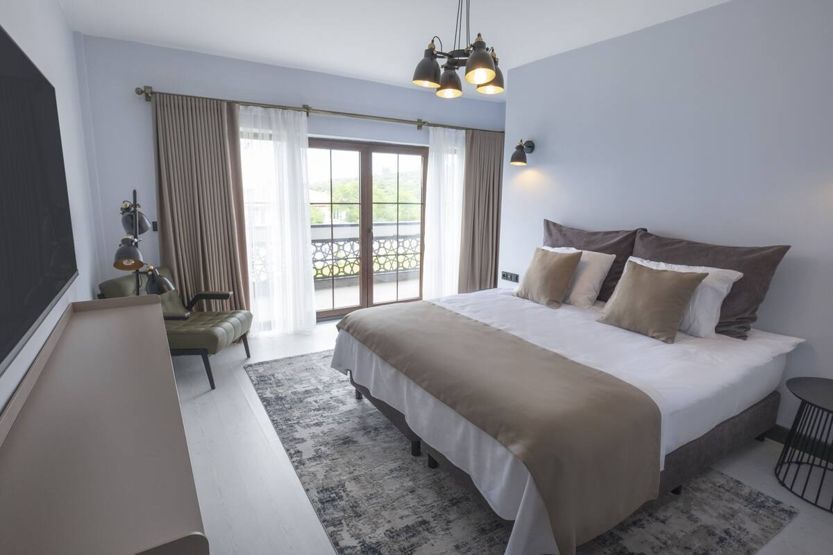 Ein modernes Schlafzimmer mit einem großen Bett, einem Balkon mit Vorhängen, einem Schreibtisch mit Stuhl und einem Fernseher.