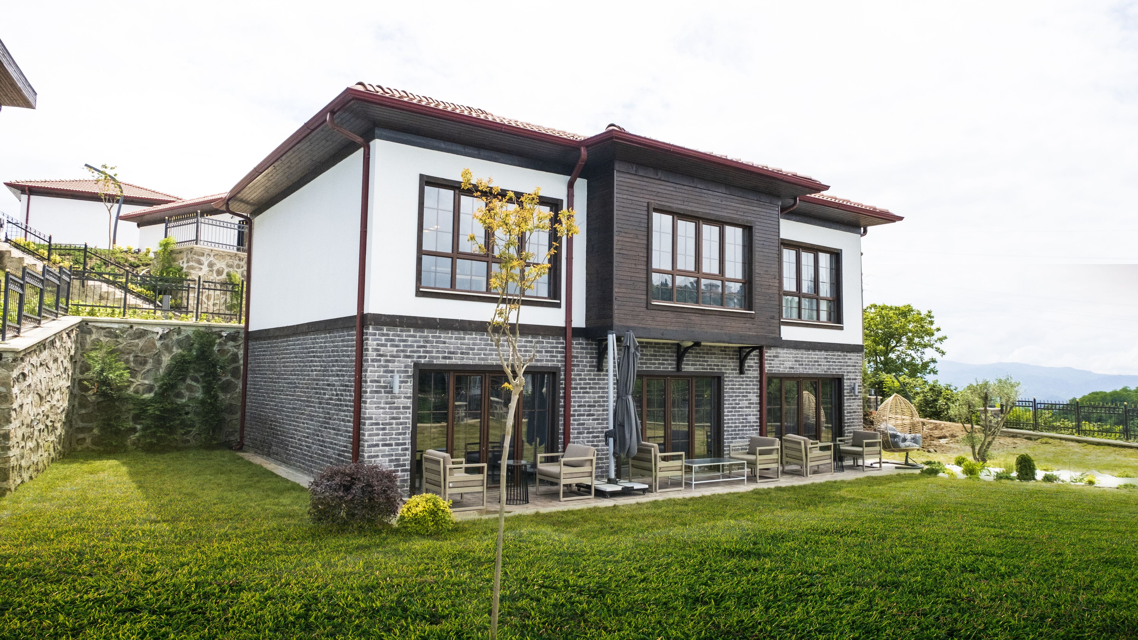 A modern two-story house with a stone facade, large windows, and a well-maintained lawn.