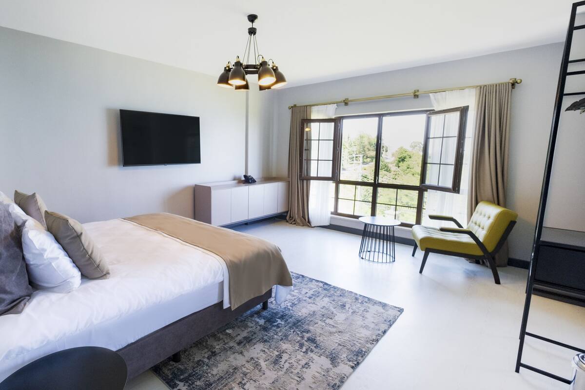 Ein modernes Hotelzimmer mit einem großen Bett, einem Flachbildfernseher, einem Schreibtisch mit Stuhl und einem großen Fenster mit Vorhängen.