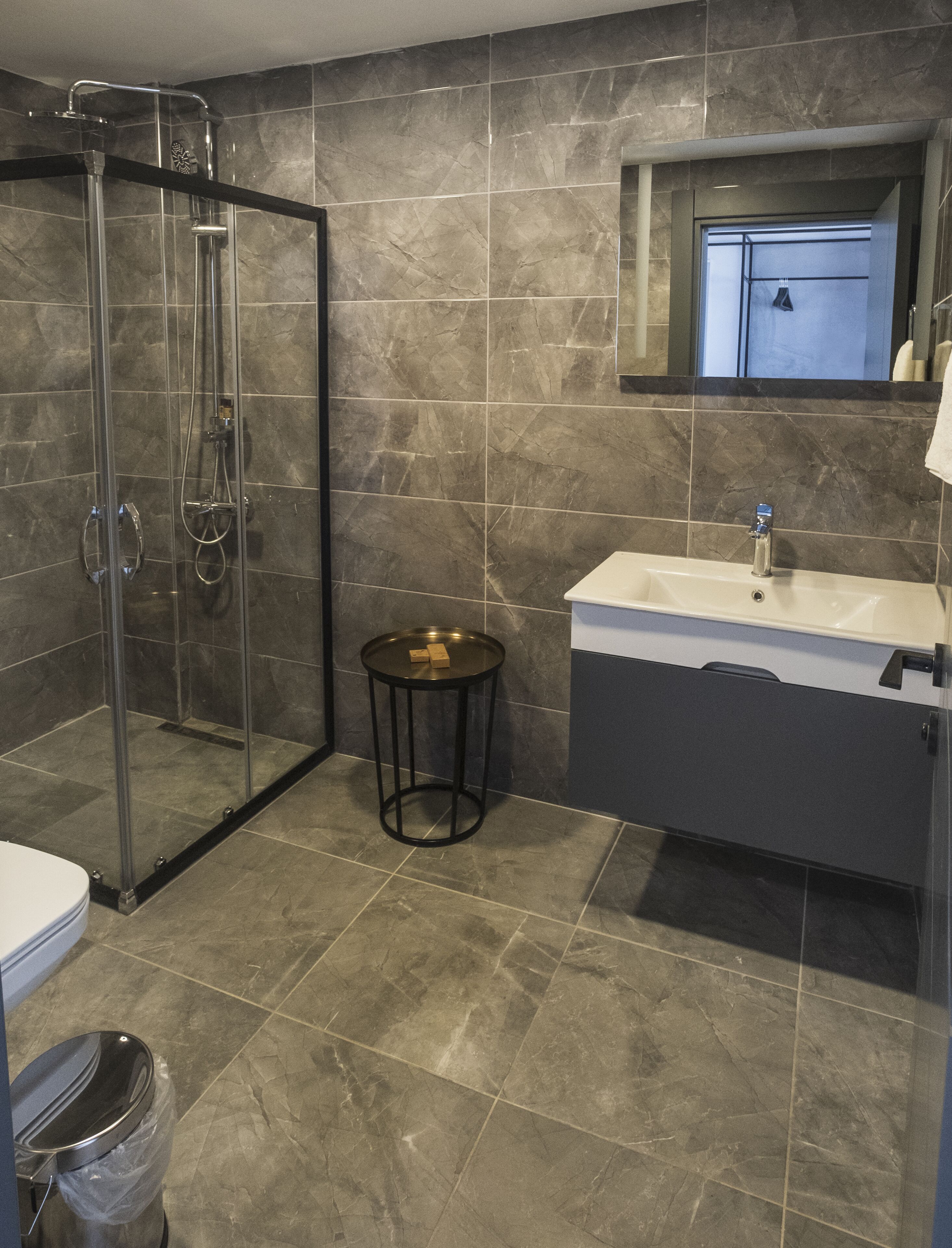 Une salle de bain moderne avec une douche à l’italienne en verre, une table ronde noire, un lavabo avec un miroir au-dessus et des toilettes.