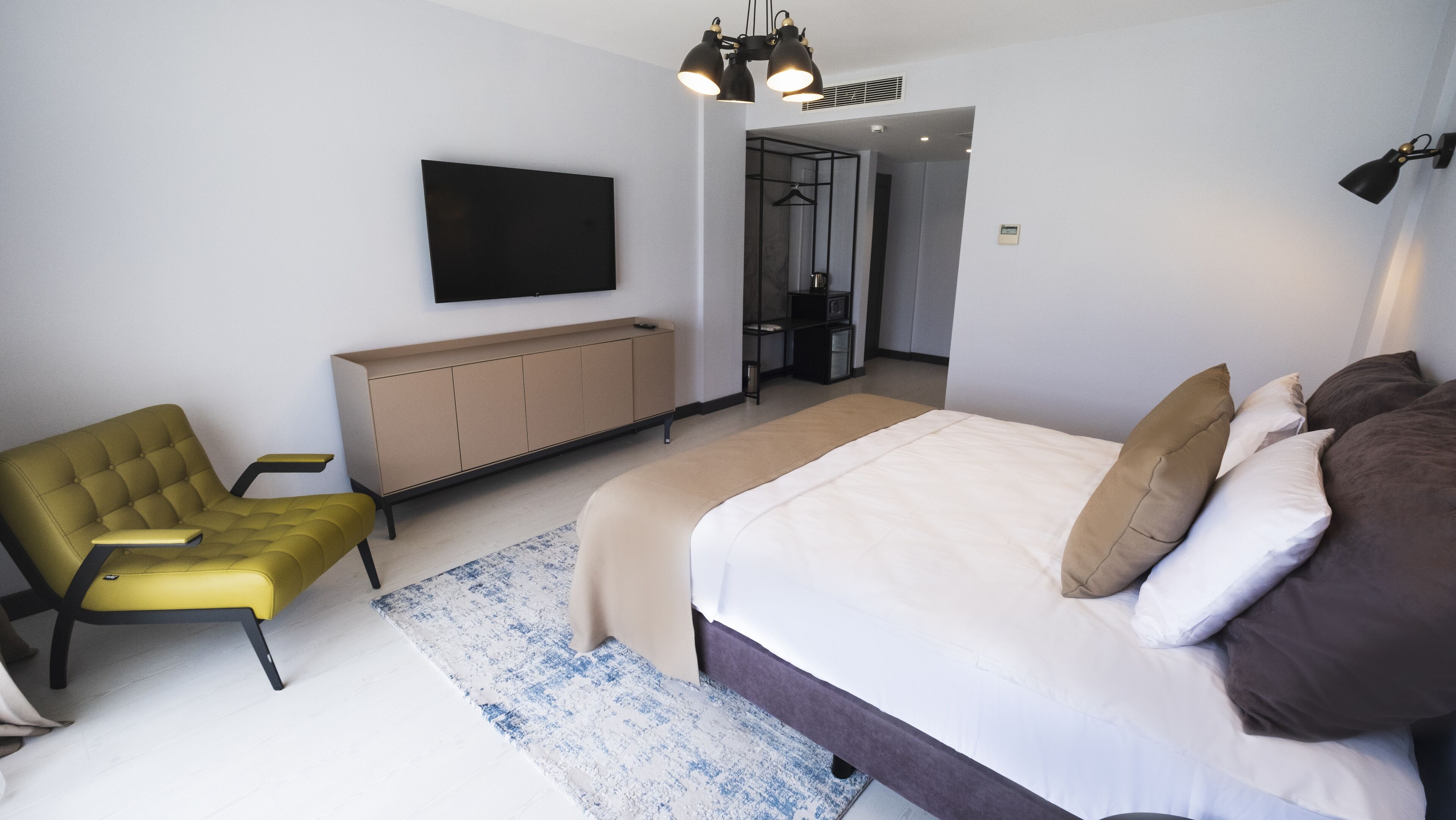 A modern bedroom with a bed, a yellow armchair, a TV mounted on the wall, and a wardrobe.