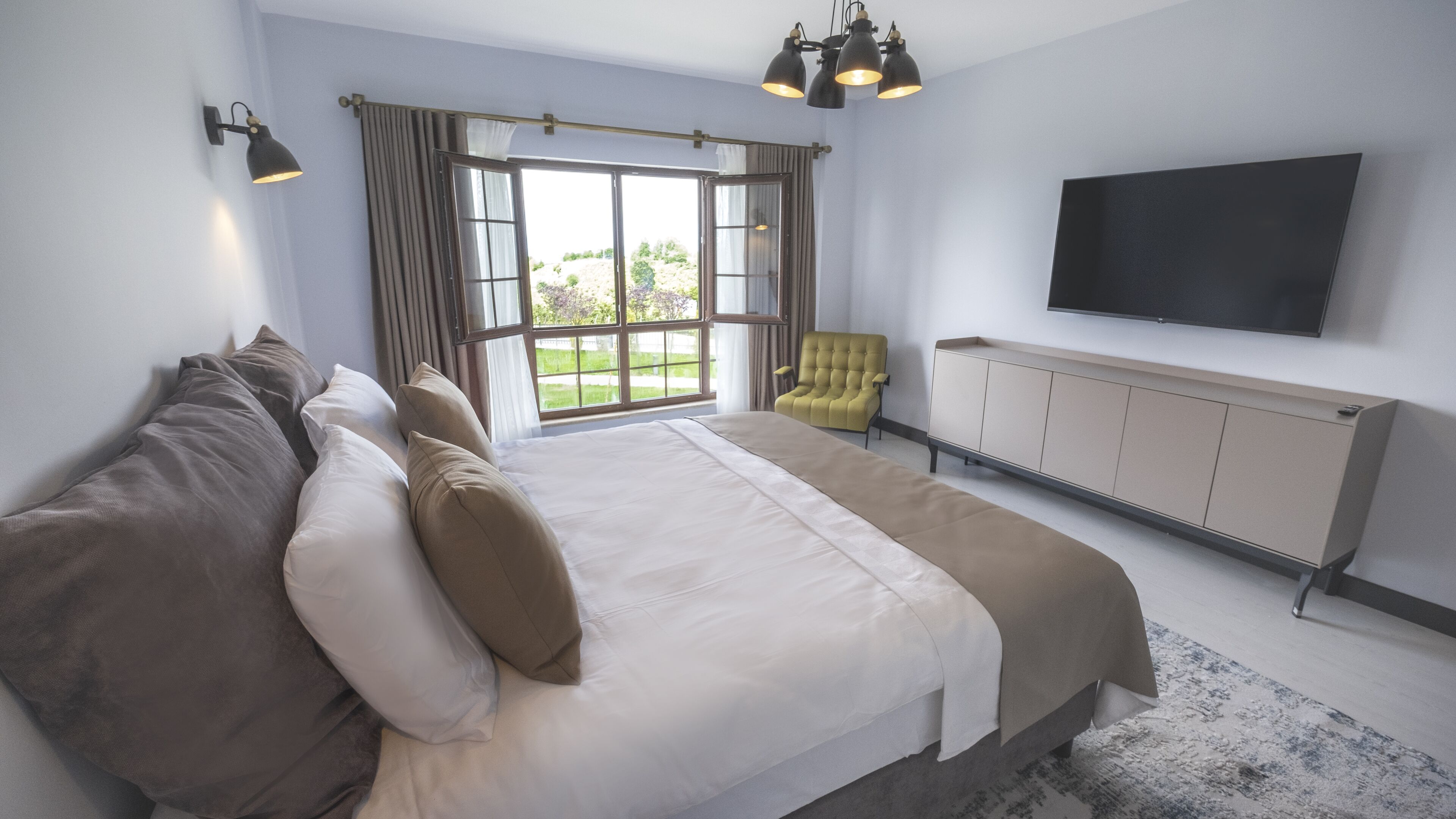 A bedroom with a large bed, a chair, a TV, and a window with curtains.
