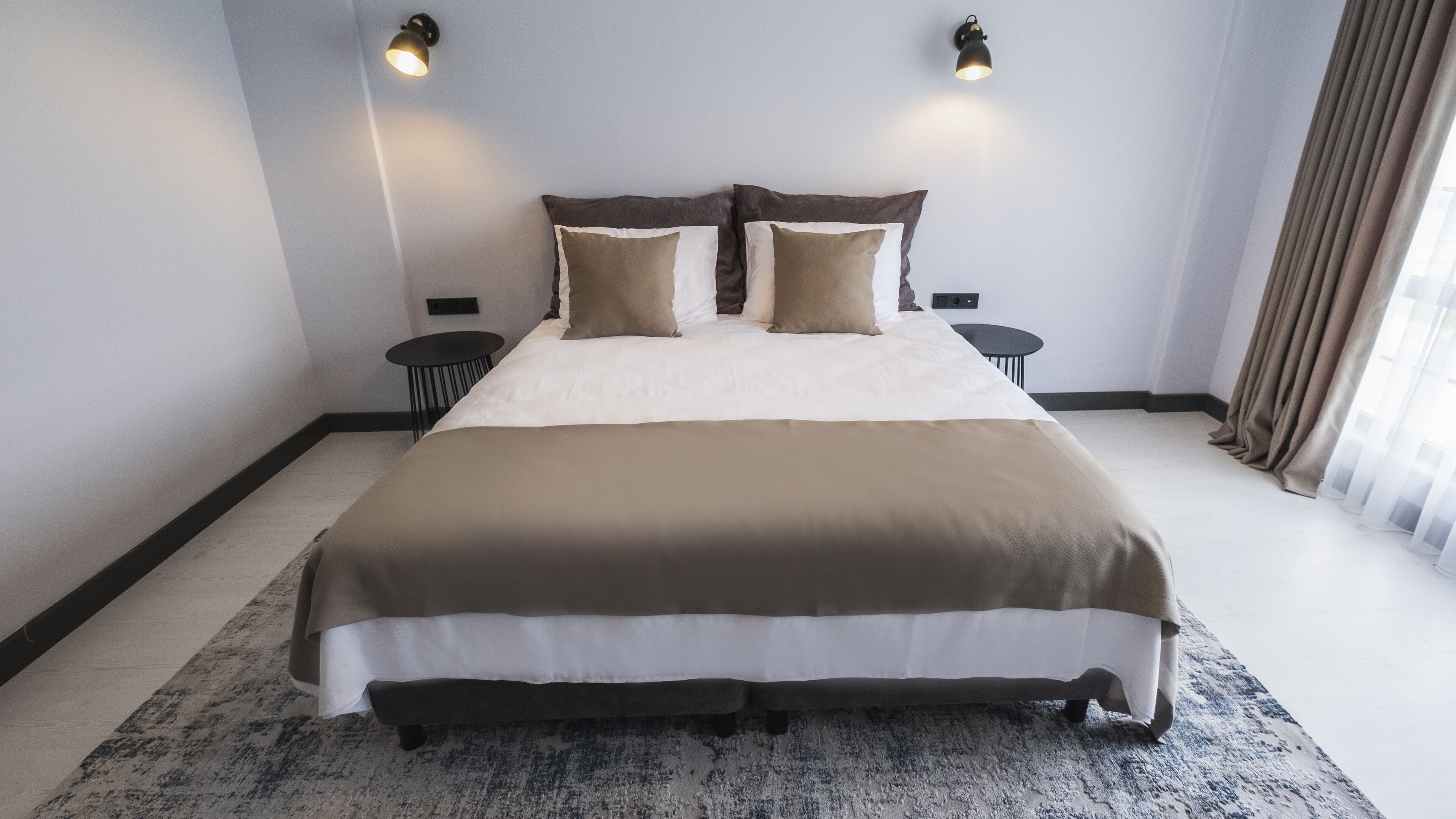 A hotel room with a large bed, two bedside tables, and a window with curtains.