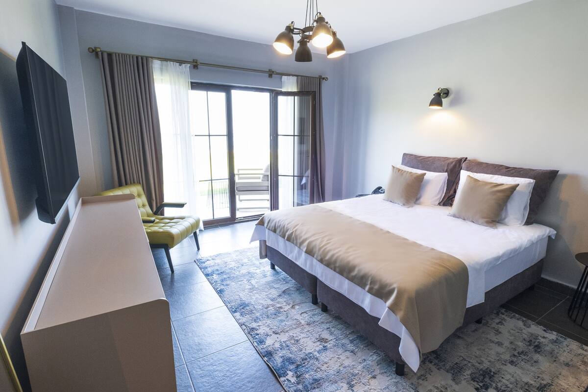 Ein Hotelzimmer mit Bett, Schreibtisch, Stuhl, Fernseher und einem Balkon mit Vorhängen.