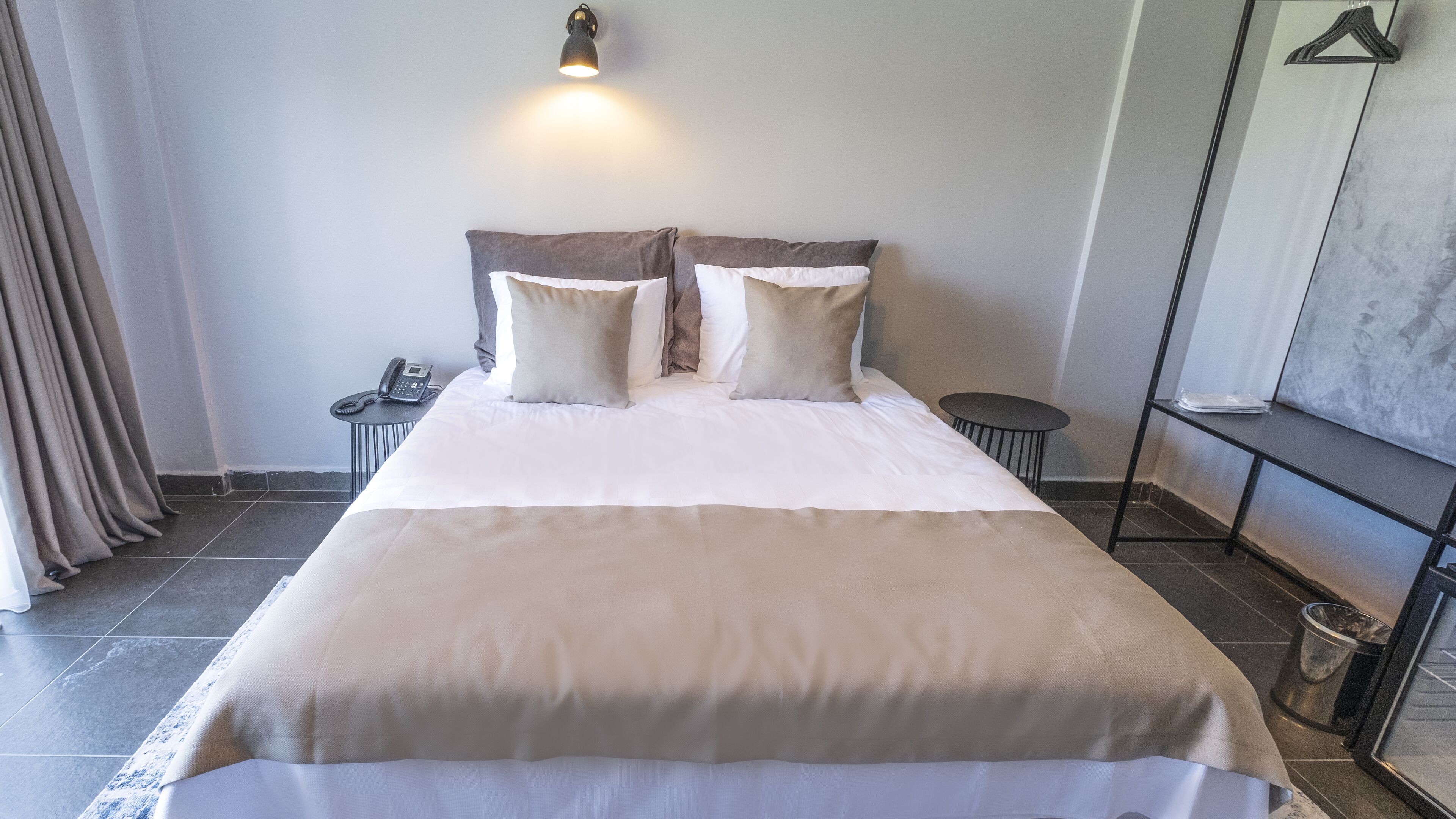 Una cama bien tendida con colcha blanca y color crema, dos almohadas, una mesita de noche con teléfono y una pequeña mesa redonda.