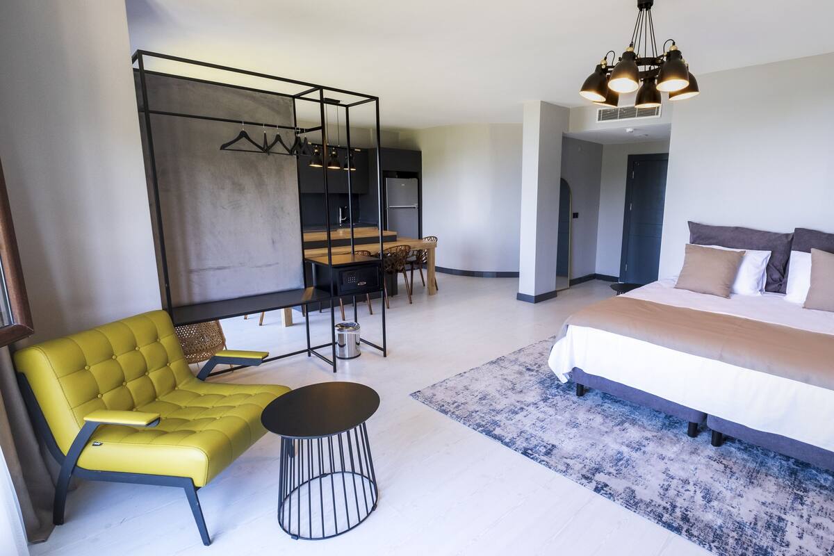 Ein modernes Hotelzimmer mit einem Bett, einem gelben Sessel, einem Esstisch und einer Pendelleuchte.