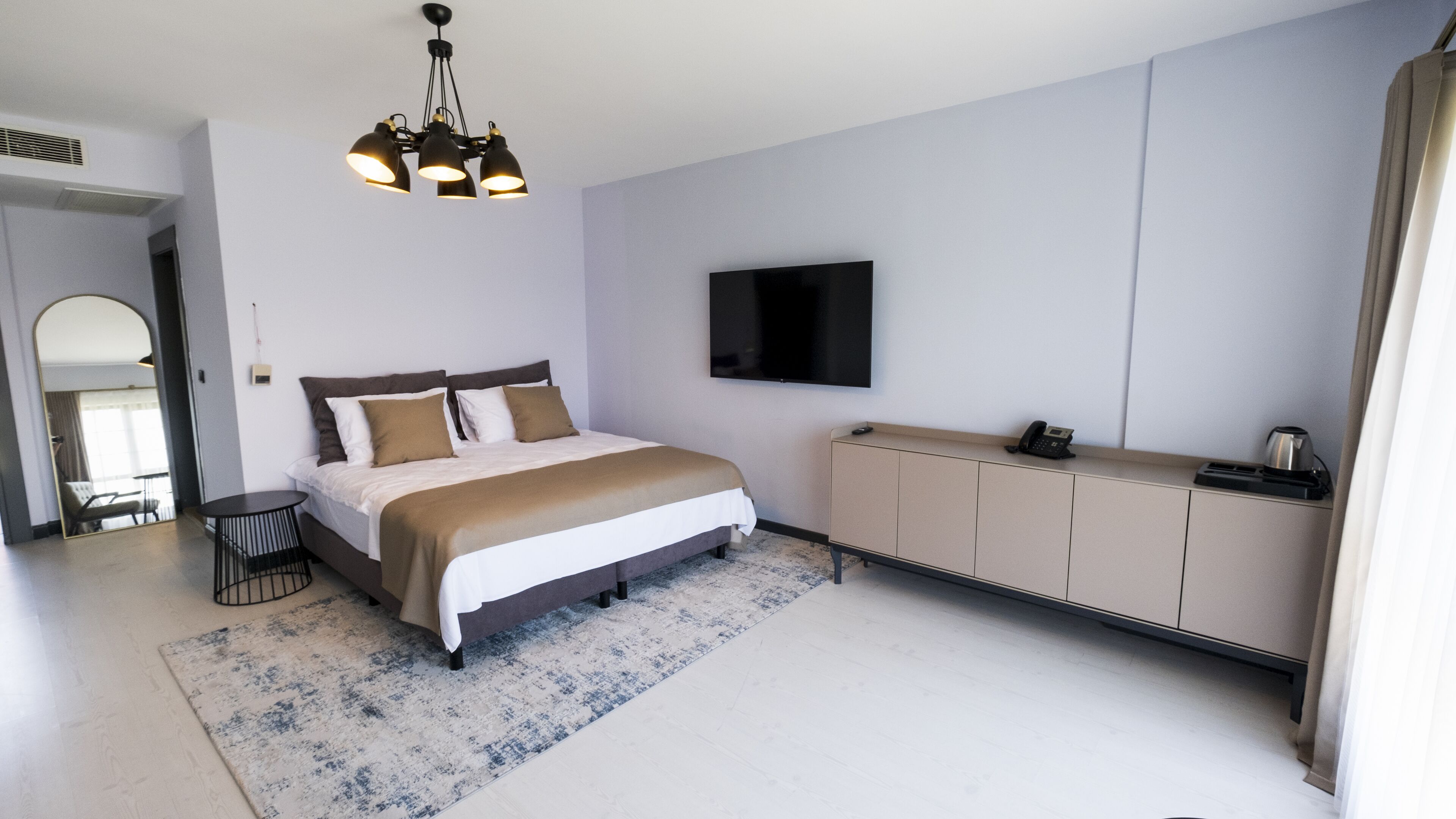 Una habitación de hotel moderna con una cama grande, un televisor de pantalla plana, un minibar y un espejo amplio.