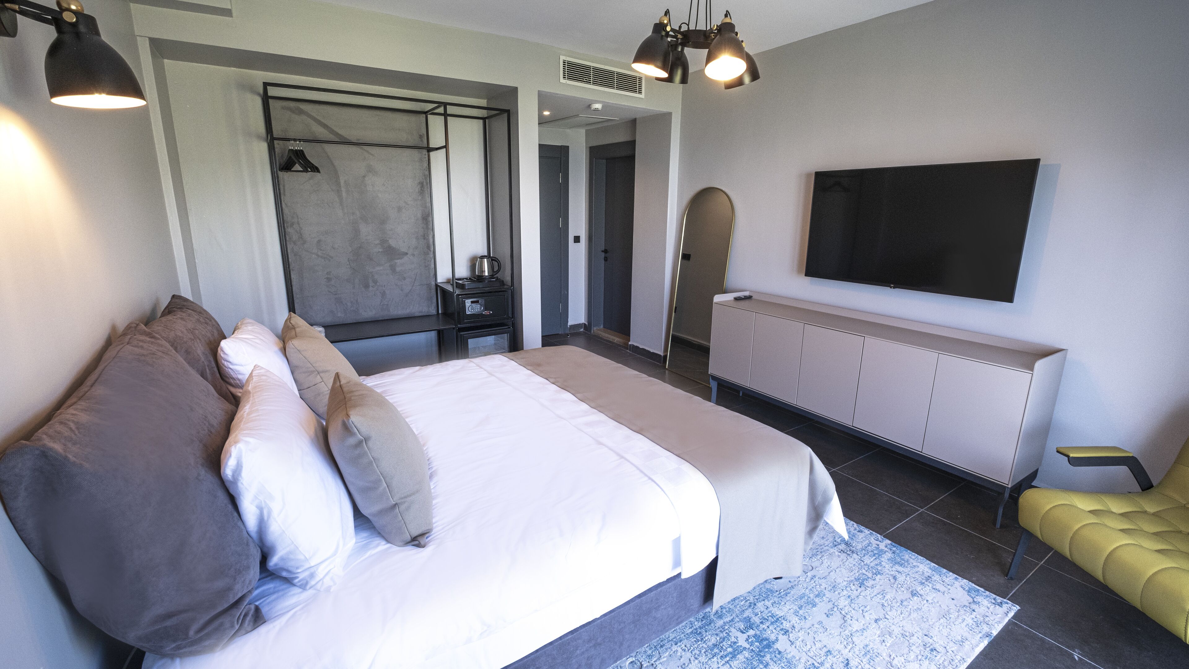A modern hotel room with a large bed, a television mounted on the wall, a seating area with a yellow sofa, and a small table.