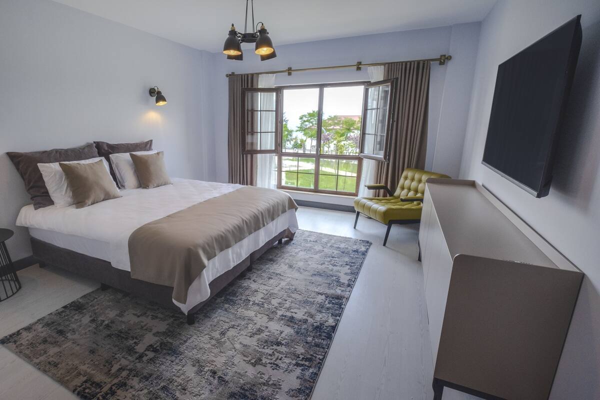 Ein modernes Schlafzimmer mit einem großen Bett, einem kleinen runden Tisch, einer Couch und einem an der Wand montierten Fernseher.