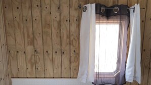 A wooden-paneled room with a bed, a window with curtains, and a pillow with a polka dot pattern.