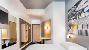 A modern hotel room with a large bed, built-in shelves, a mirror, and a wall-mounted light. - B&B HOTEL Gießen-City (Giessen)