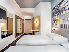Habitación de hotel moderna con una cama grande, estantes integrados, un espejo y una lámpara fijada a la pared.