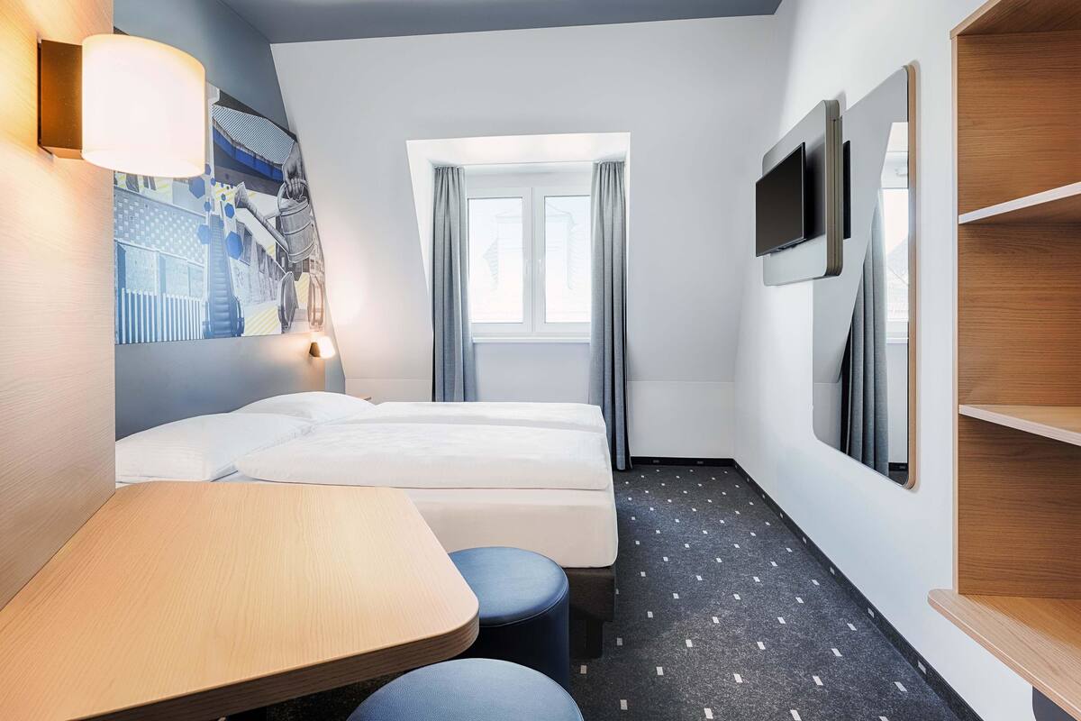 A hotel room with a bed, a desk, a chair, a TV, and a window with curtains.