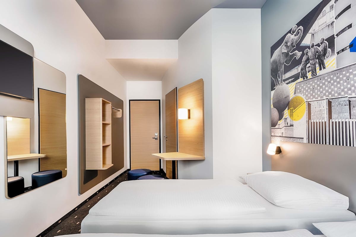 A modern hotel room with a large bed, built-in shelves, a mirror, and a wall-mounted light.