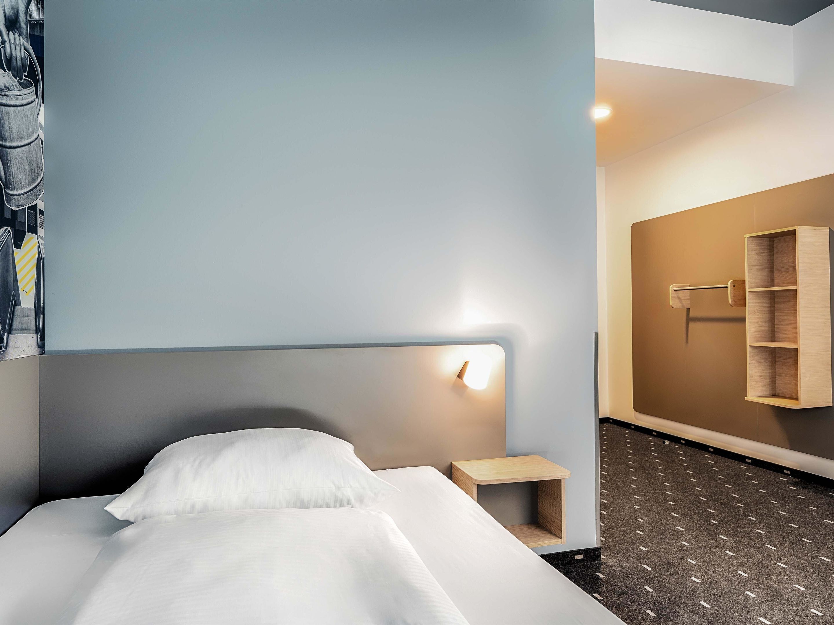 Ein modernes Hotelzimmer mit Bett, Nachttisch, Wandregal und einem Gemälde an der Wand.