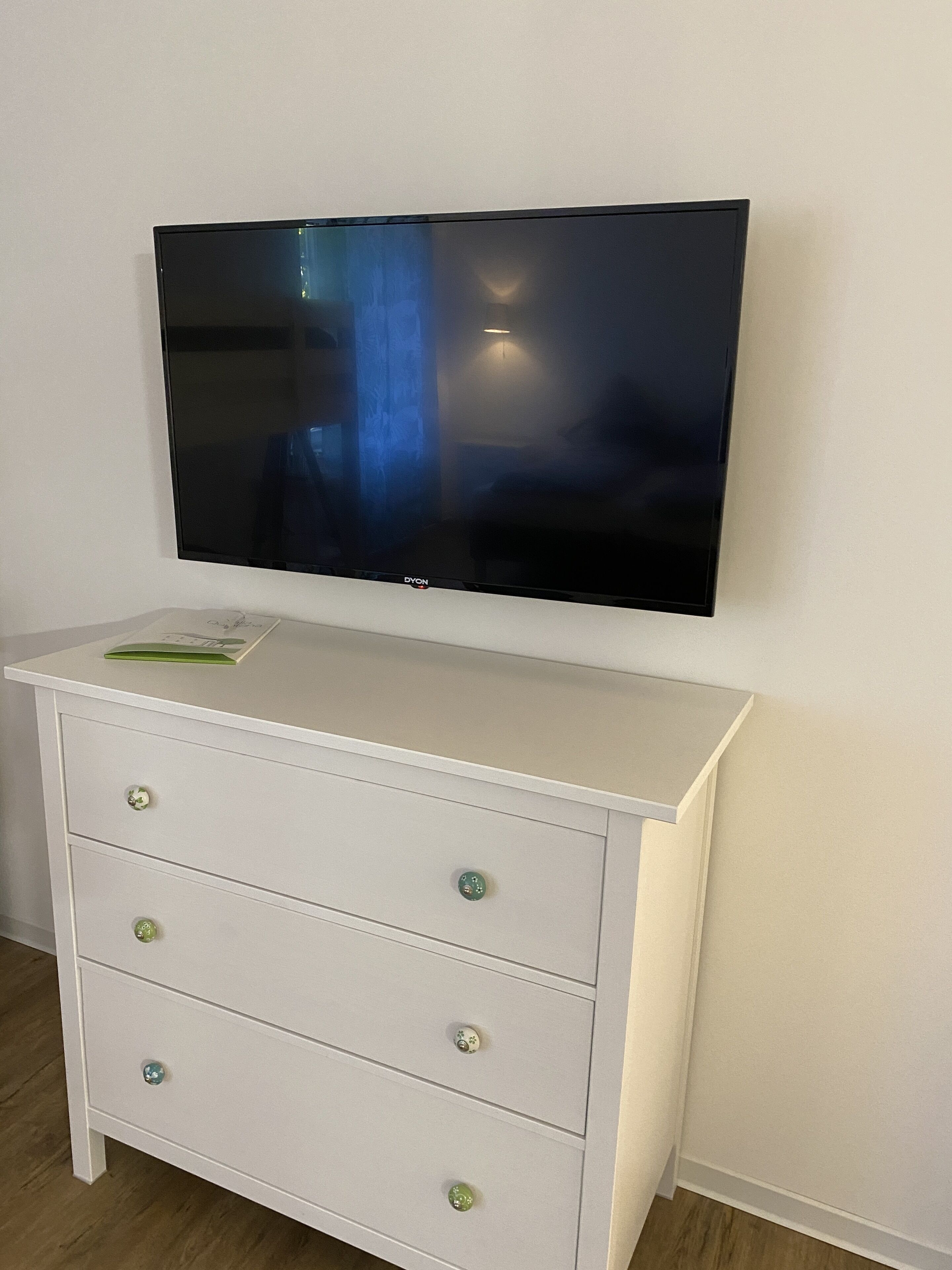 Un televisor de pantalla plana montado sobre un aparador blanco de tres cajones, cada uno con una perilla verde.