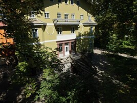 Um edifício de vários andares com entrada central, rodeado por vegetação densa.