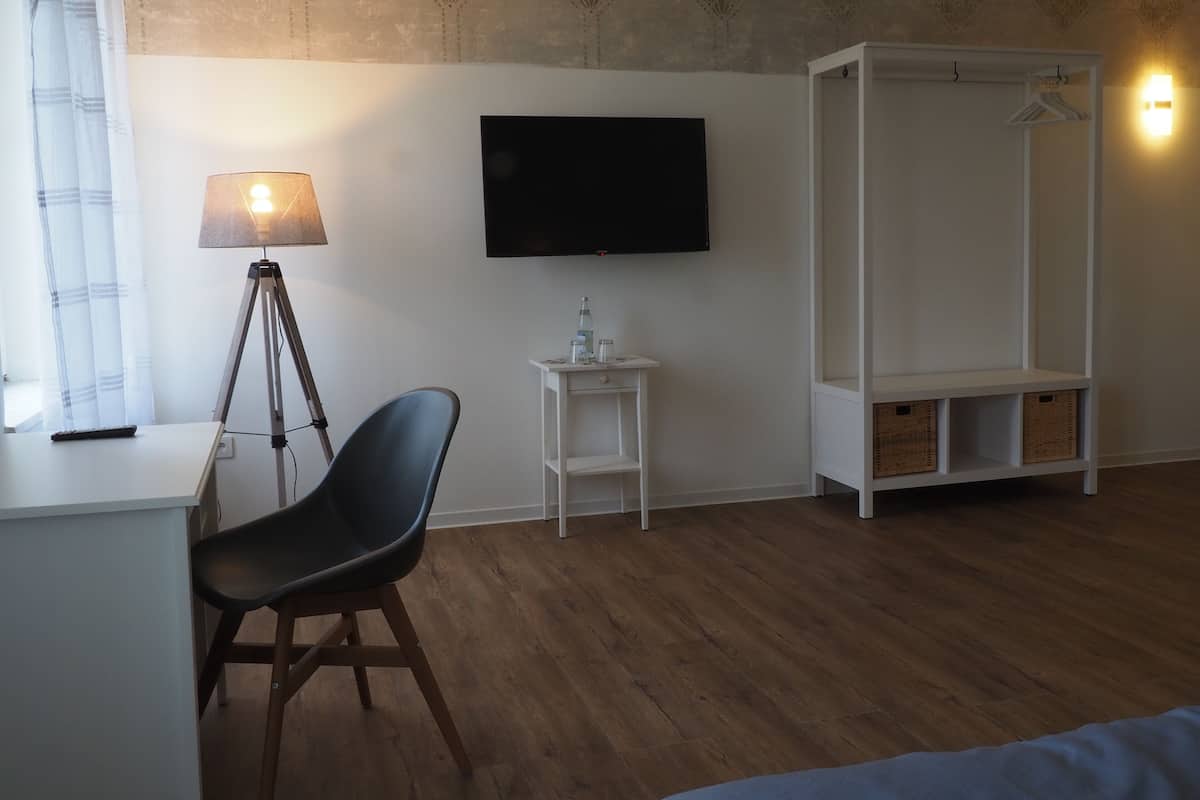 Quarto com escrivaninha, cadeira, luminária, televisão, guarda-roupa e estantes.