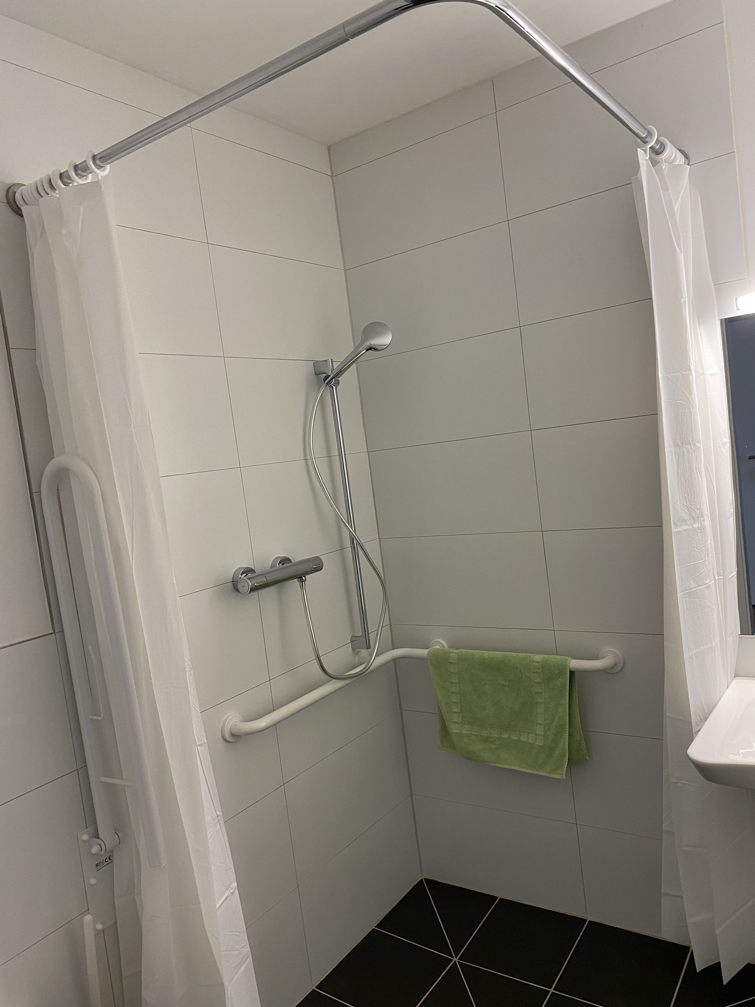 A bathroom with a shower, a green towel, and a white sink.