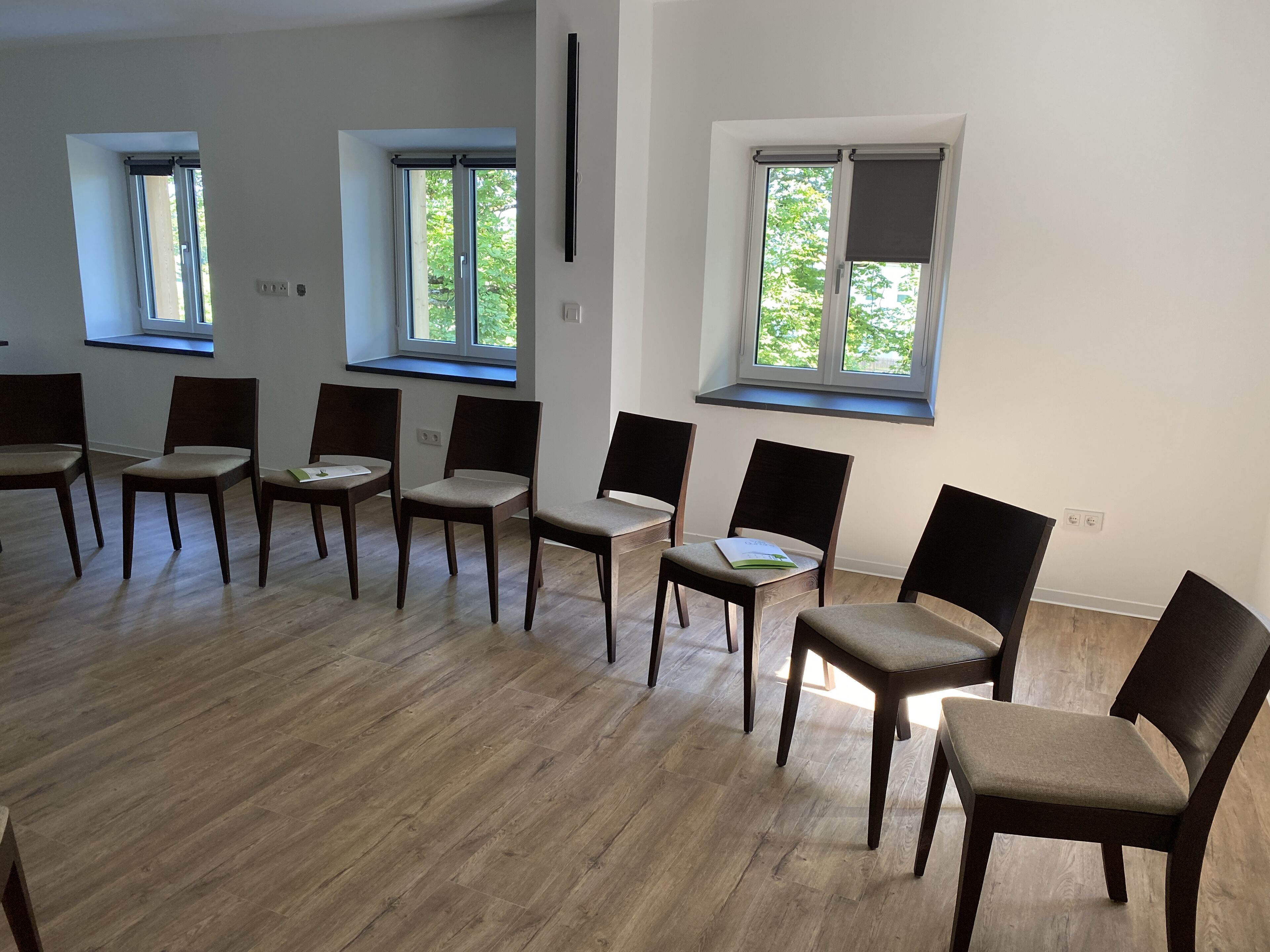 Una habitación con piso de madera, varias ventanas y varias sillas dispuestas en semicírculo.