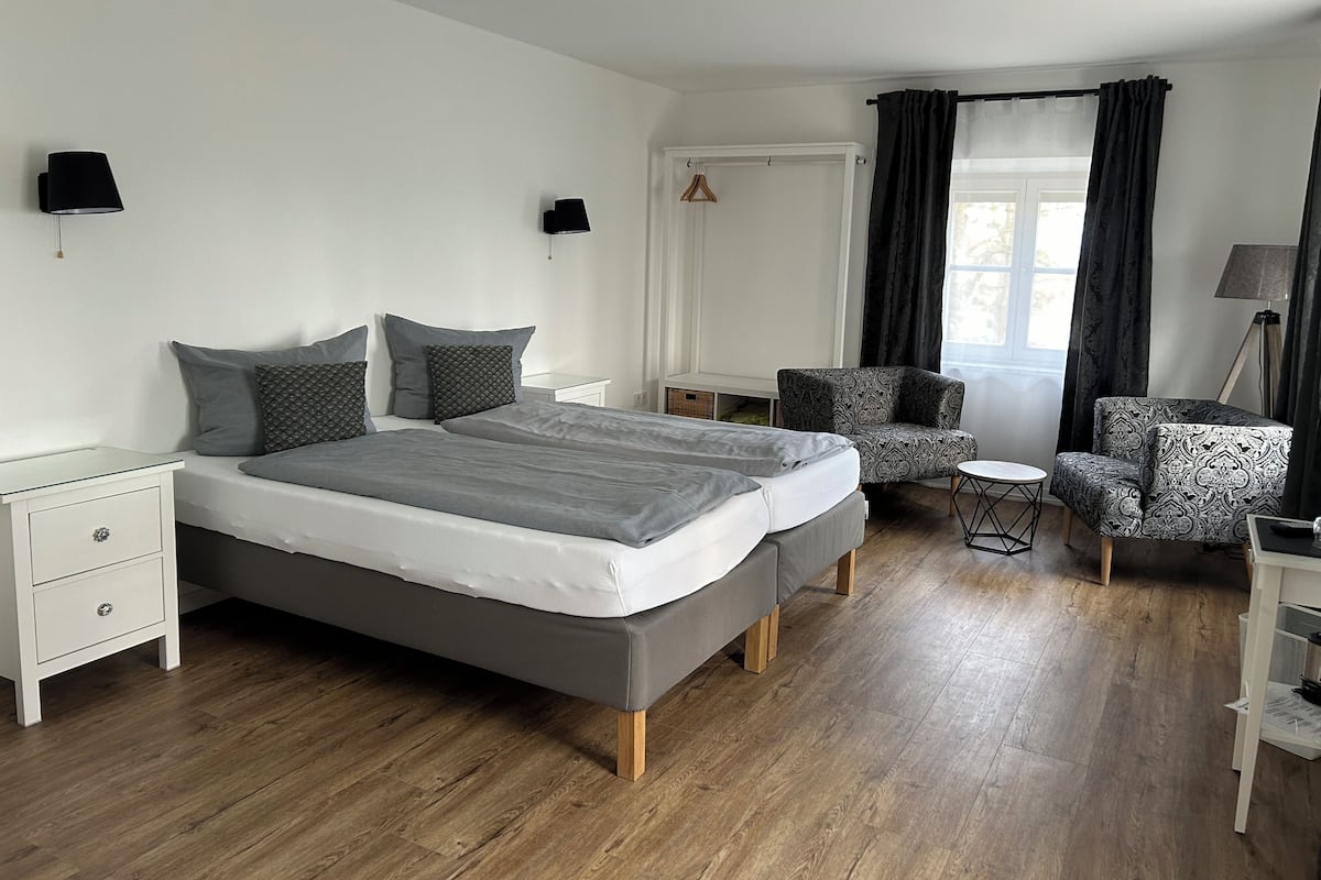 Um quarto moderno com uma cama de casal, mesas de cabeceira, uma cadeira, uma mesinha e um abajur.