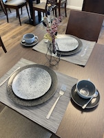 Uma mesa de jantar posta com pratos, talheres e um vaso decorativo.