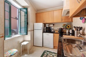 A compact kitchen with a refrigerator, microwave, sink, and a small stool.