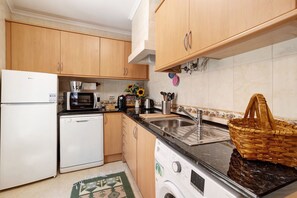 A compact kitchen with wooden cabinets, a white refrigerator, a dishwasher, a microwave, a sink, and a washing machine.