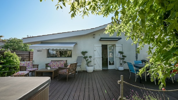 Eine Holzterrasse mit Gartenmöbeln, einem überdachten Sitzbereich und Topfpflanzen.