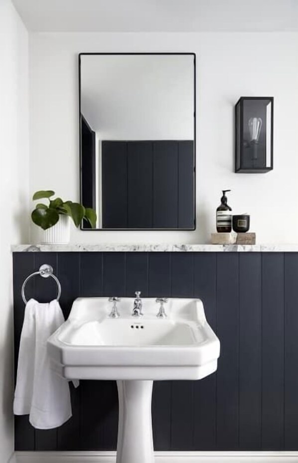 A bathroom with a white sink, dark wooden paneling, a mirror, a potted plant, and a framed picture. - Stylish Apartment minutes from Angel Tube (London)